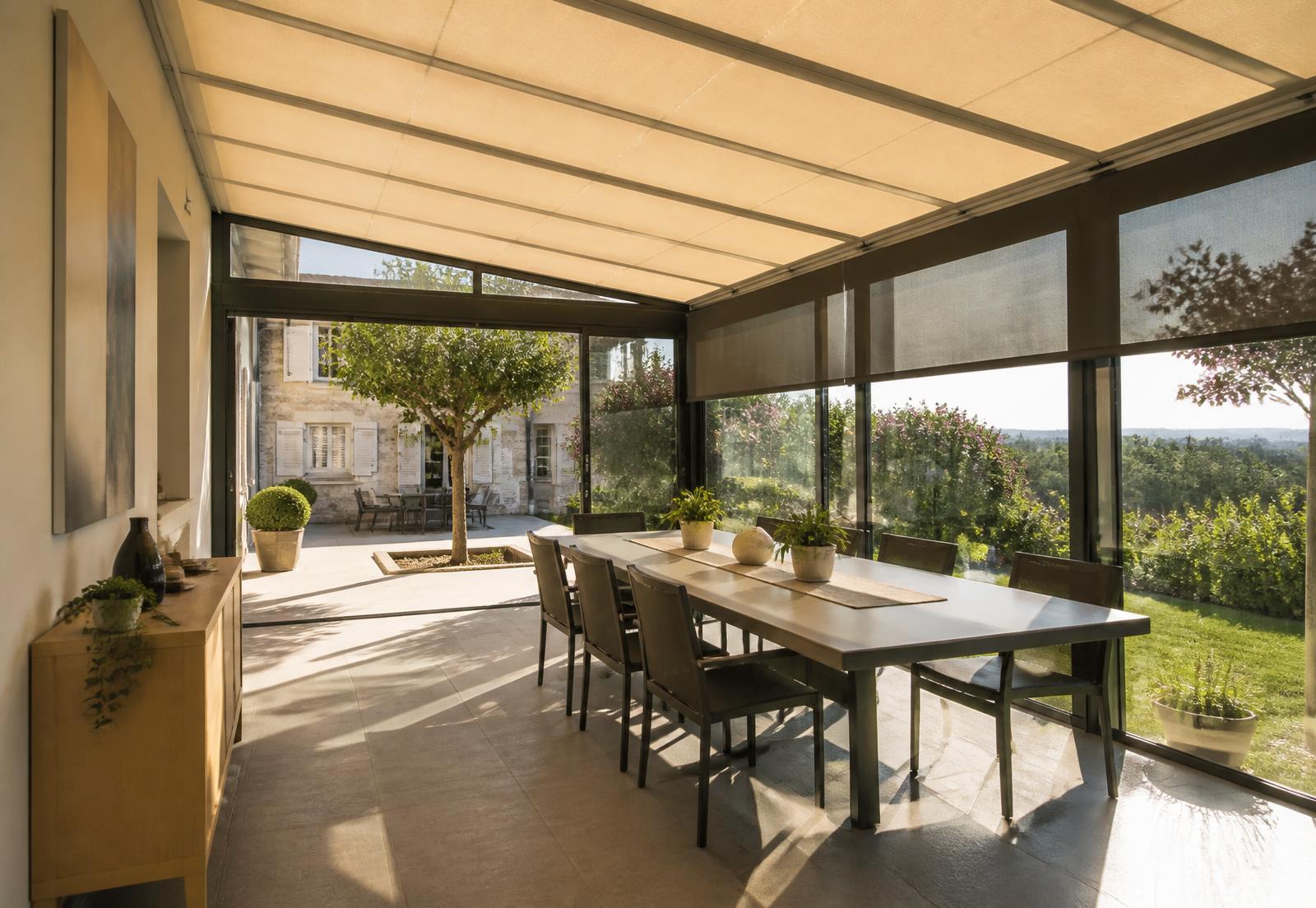 Store de véranda beige installé sur une véranda vitrée baignée de soleil